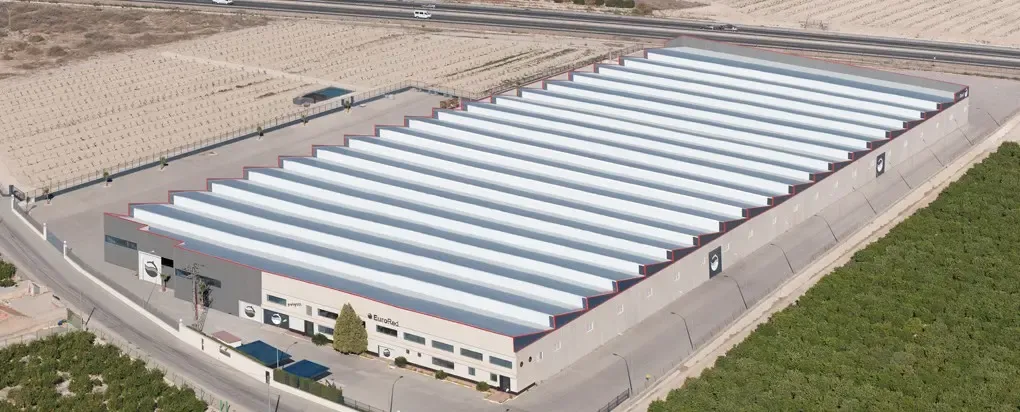 Venta de la empresa EURORED en Alicante. Líder mundial en la fabricación de redes Planta industrial con techo de chapa metálica y área de estacionamiento.