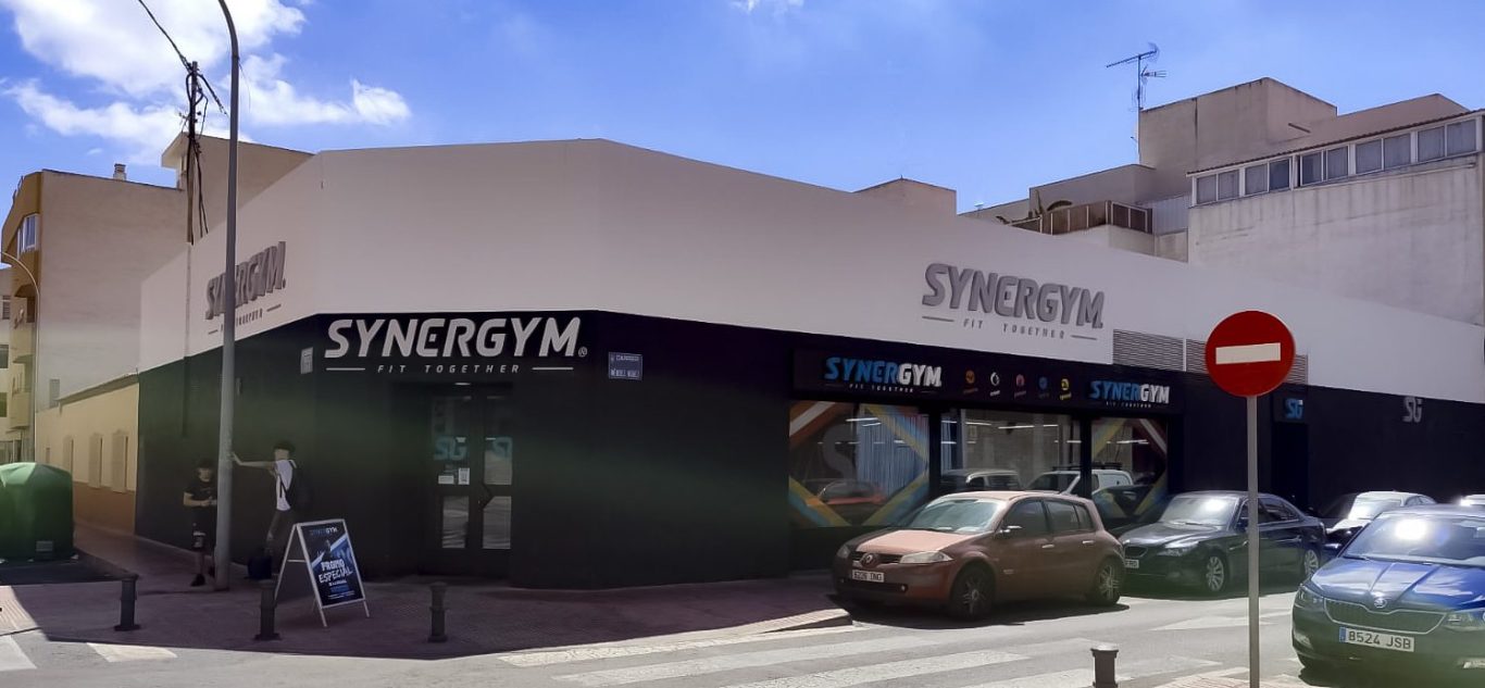 SYNERGYM en SanVicente del Raspeig Edificio de gimnasio con fachada moderna y un cartel SYBERGYM grande en la entrada.