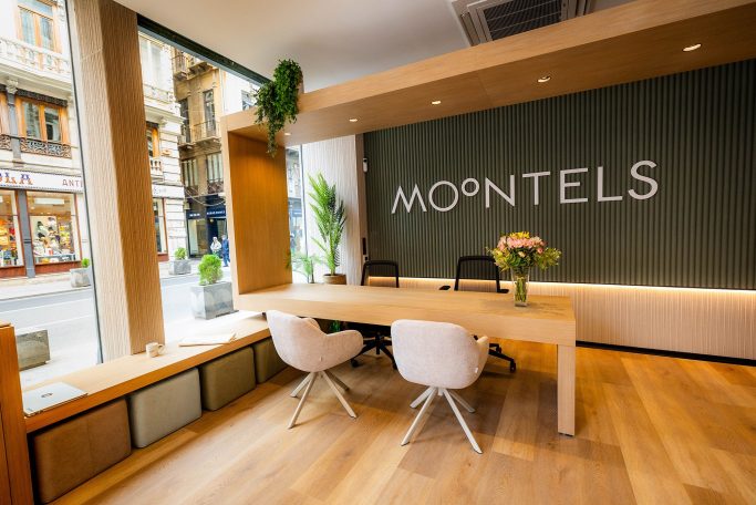 Intermediación en la compraventa de un hotel en Alicate centro para la cadena de hoteles Moontels Recibidor moderno con mesa de madera, sillas blancas y un cartel que dice "MOONTELS".